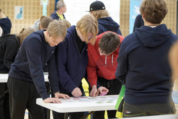 Kolme kilpailijaa kumartuneena kilpailutehtävän ääreen.