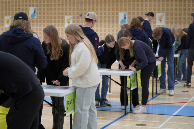 Kilpailevia joukkueita liikuntasalissa pöytien ääressä.